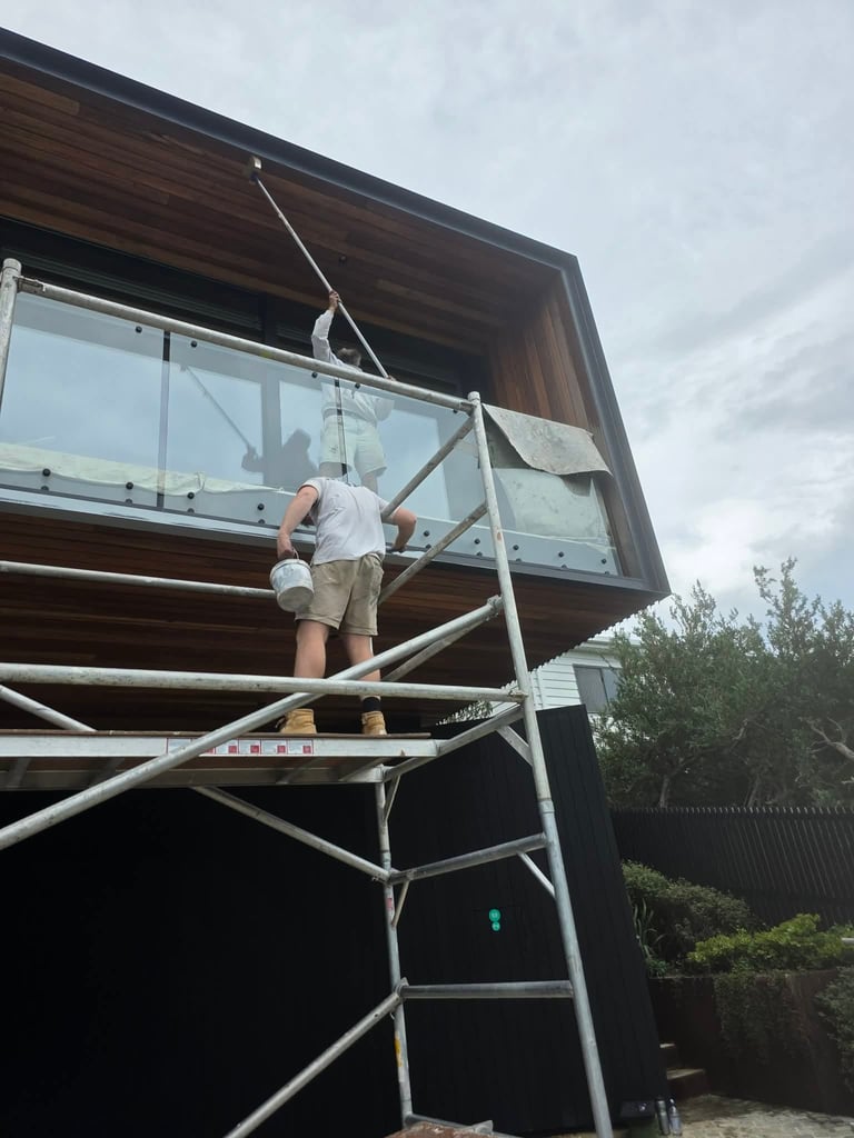Worker in white shirt on metal scaffolding installing window on modern dark wood building under cloudy sky