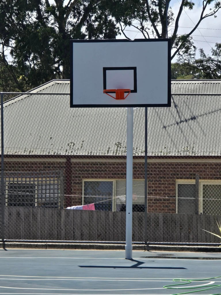 Basketball hoop and backboard on outdoor court with brick building and metal fence in background