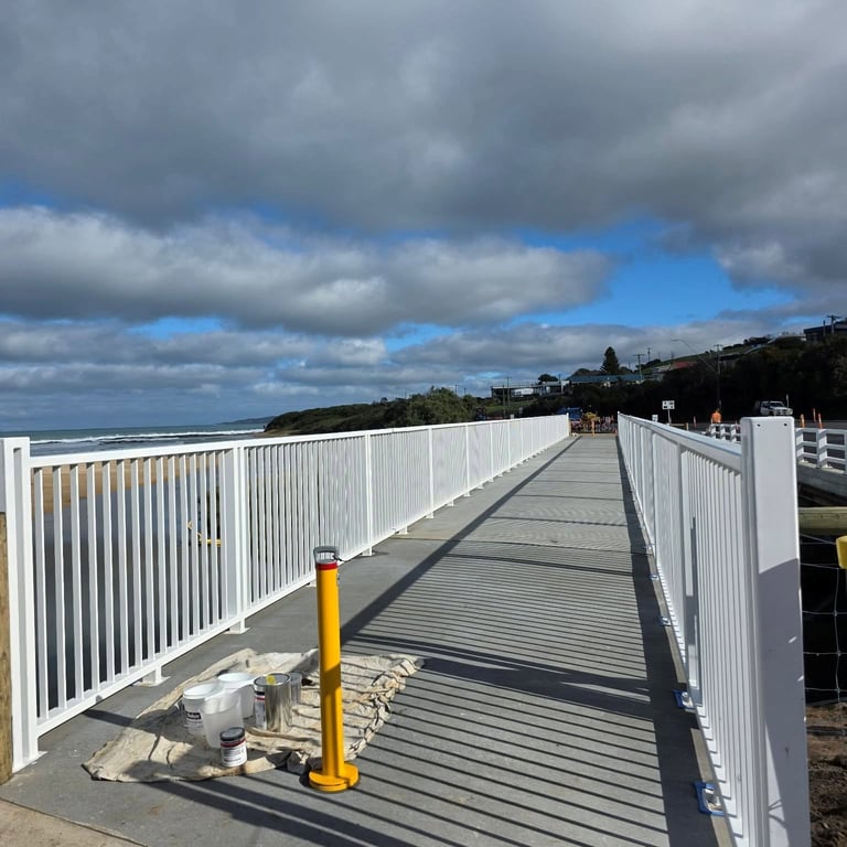Metal footbridge with white railings spanning across industrial area under cloudy sky