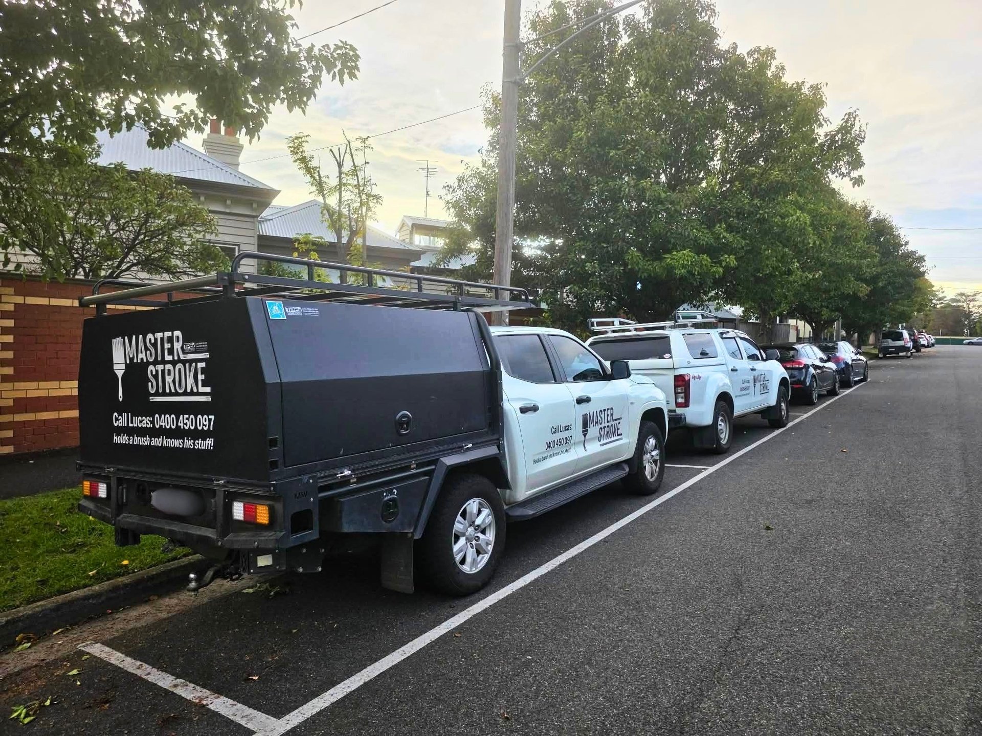 Row of Master Stroke service vehicles parked on a street, including a black van and white utility trucks