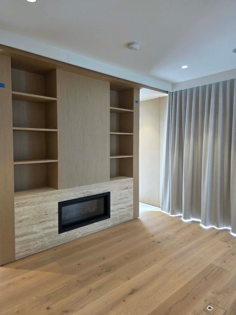 Modern living room with built-in wooden shelving unit, fireplace insert, and light wood flooring under ambient ceiling lights