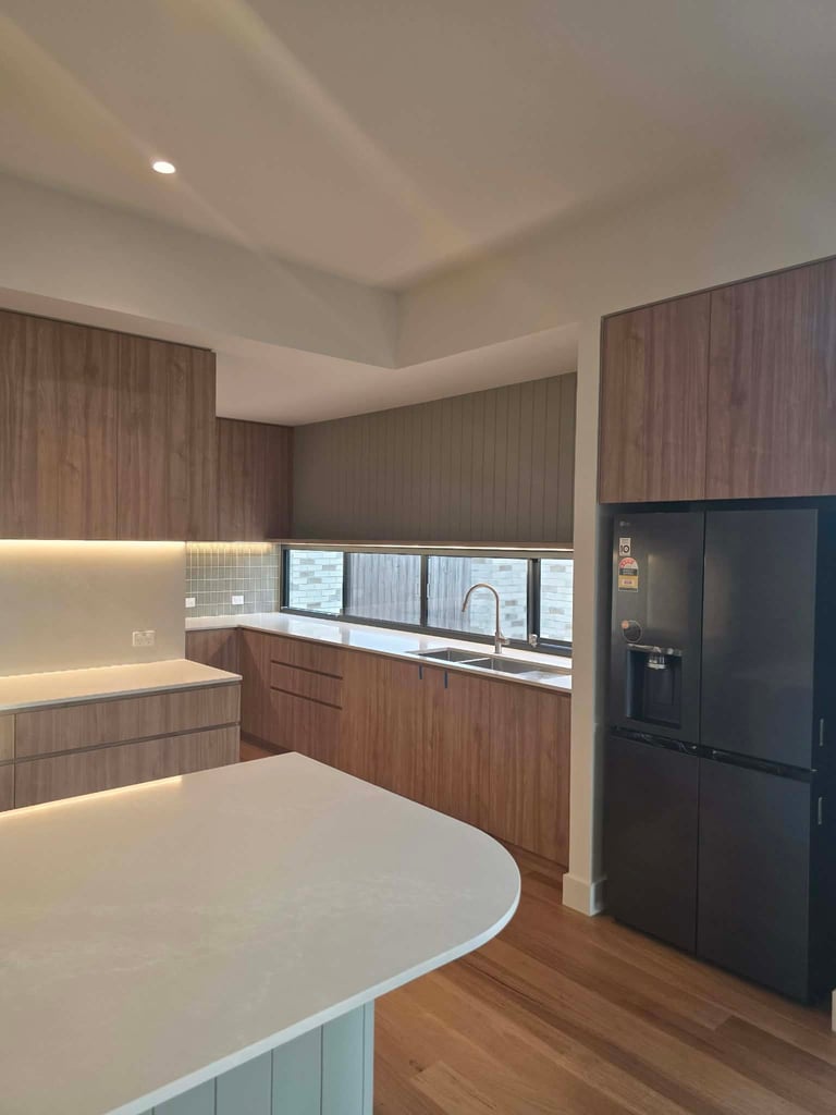 Modern kitchen with brown wood cabinetry, white countertops, island seating, black refrigerator, and recessed ceiling lighting