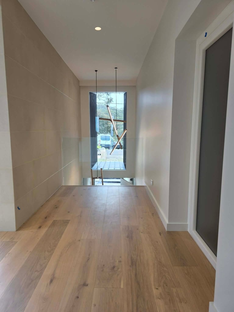 Modern hallway with wood flooring, white walls, recessed lighting, and large window at far end