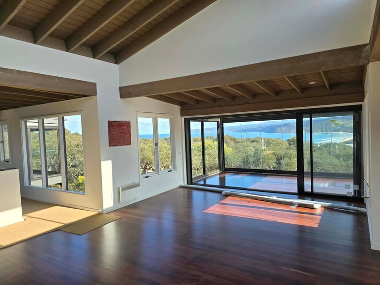 Modern open-plan interior with dark hardwood floors, exposed wooden beams, large windows overlooking mountains and landscape