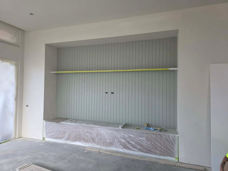Empty room with white walls and a built-in shelving unit with vertical ribbed backing and protective plastic sheeting.