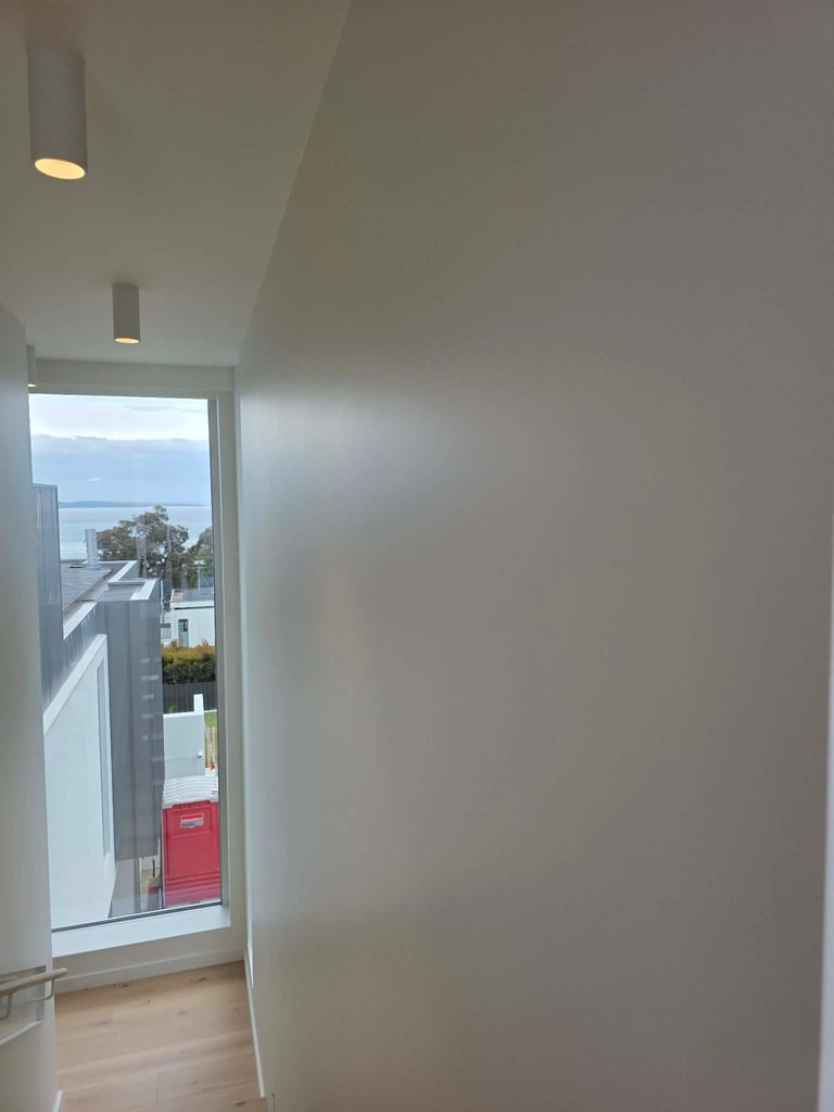 Modern hallway with recessed ceiling lights and a large window overlooking a coastal landscape with water and trees