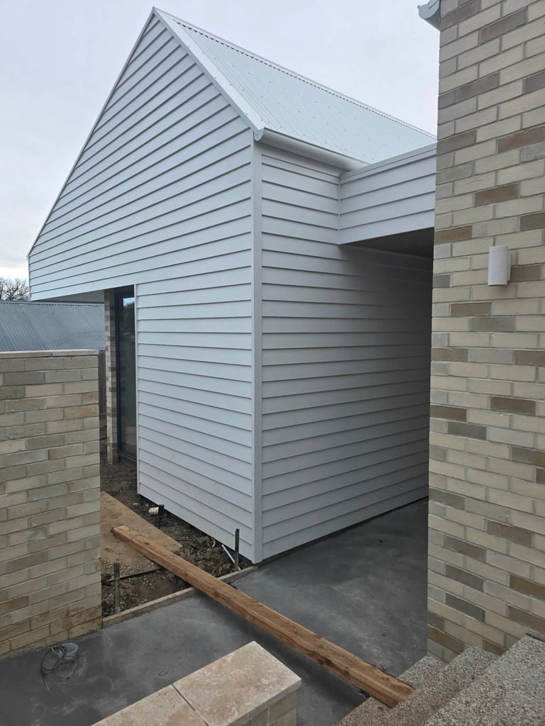 Modern light blue metal-sided garden shed attached to brick house with pitched roof