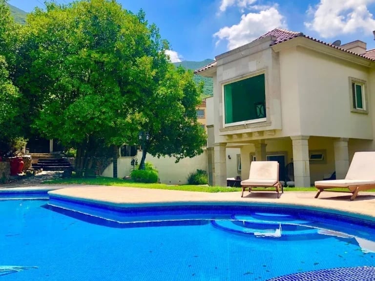Modern house with swimming pool, lounge chairs, green shutters, and mature trees on sunny day
