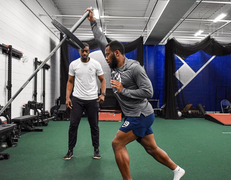 Personal trainer in white shirt observing athlete performing plyometric training exercise in modern gym