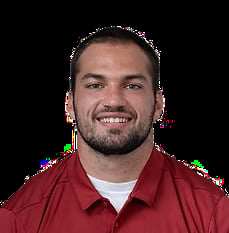 Professional headshot of a smiling man with dark hair and beard wearing a burgundy polo shirt
