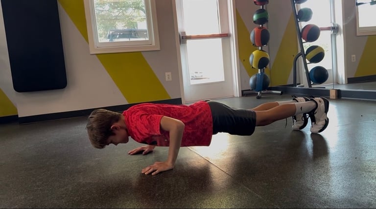Young athlete in red shirt doing a plank exercise on gym floor with medicine balls and weights