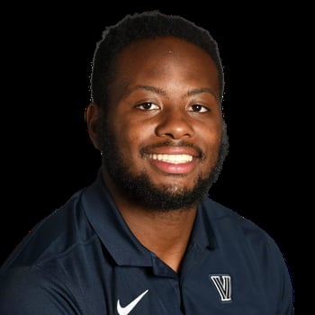 Smiling man wearing dark Nike polo shirt with Villanova logo against black background