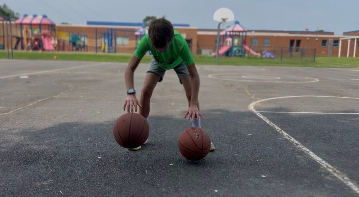 Athlete in green shirt performing push-up while balancing on two basketballs on outdoor court