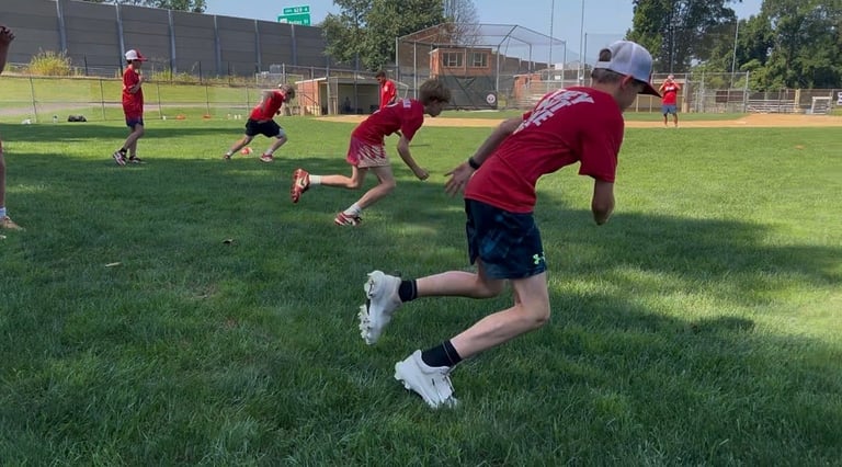 Young baseball player in red uniform sprinting during practice on a sunny field with teammates in background
