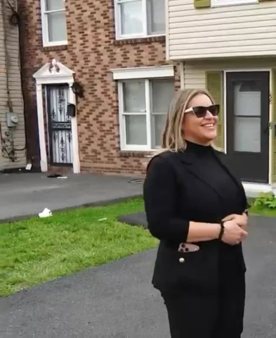 Argeli en blazer negro y gafas de sol frente a su nueva casa después de reparar su crédito con Dotel Group