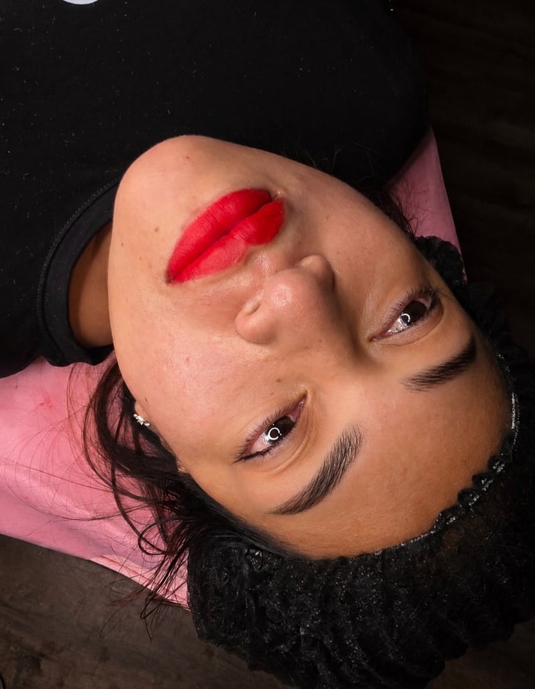 Person with head tilted back wearing bold red lipstick, dramatic eye makeup, and a pink top against a dark background