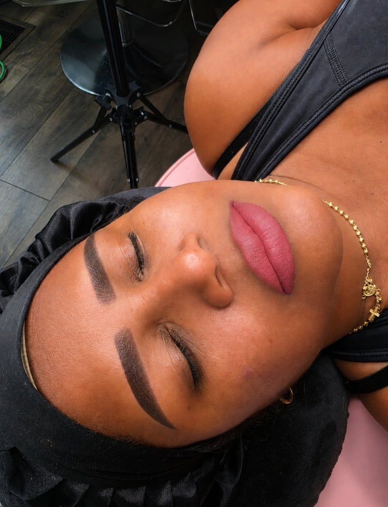 Woman wearing makeup with defined eyebrows, burgundy lipstick, and gold beaded bracelet, lying down indoors