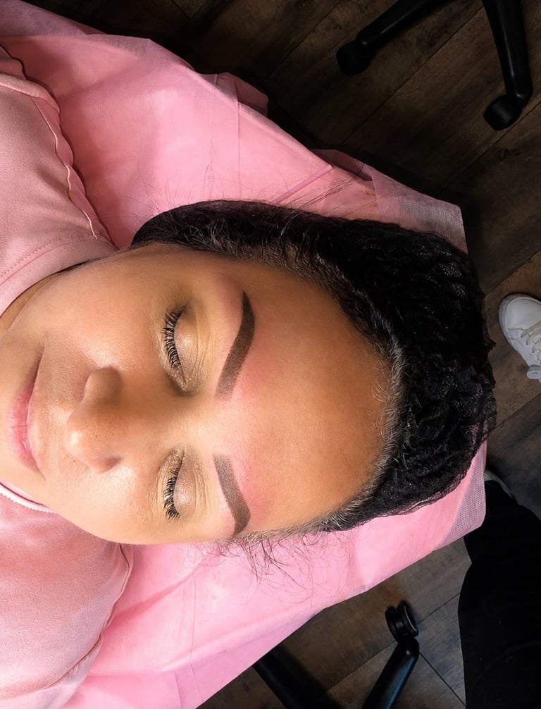 Person with eyes closed wearing pink fabric, showing sculpted eyebrows and natural makeup in overhead view