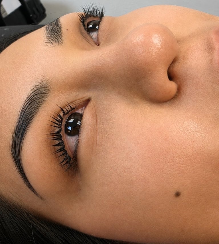 Close-up of a womans face showing professionally styled eyebrows and voluminous black eyelashes with glossy eye makeup