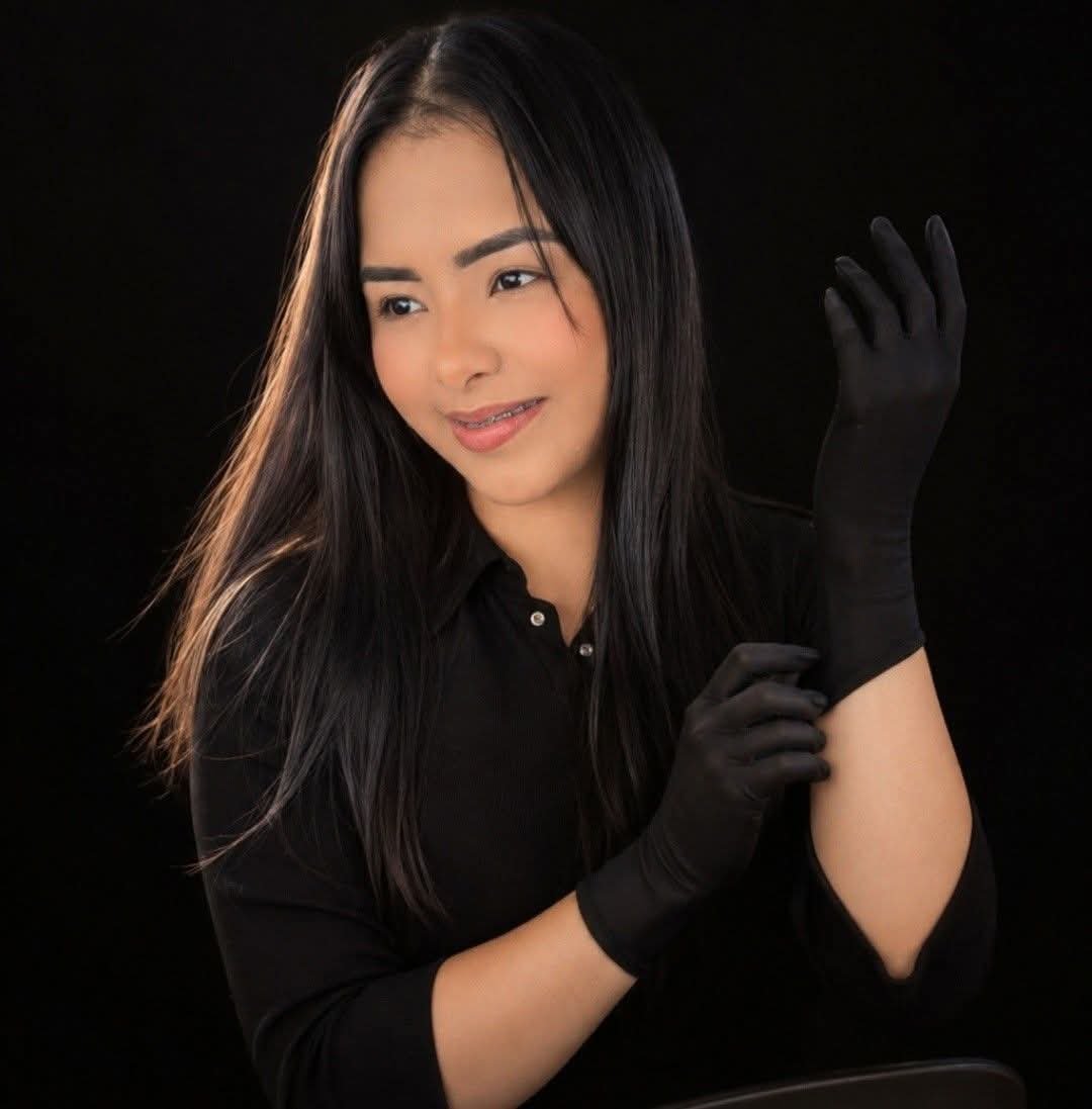 Woman with long black hair wearing black gloves and black top, posing against dark background