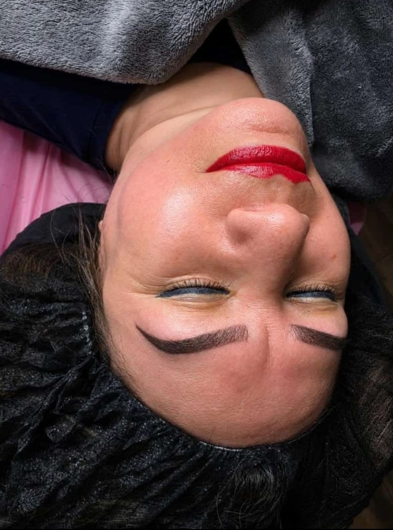 Persons face upside down wearing red lipstick and dark eye makeup, surrounded by gray and black clothing