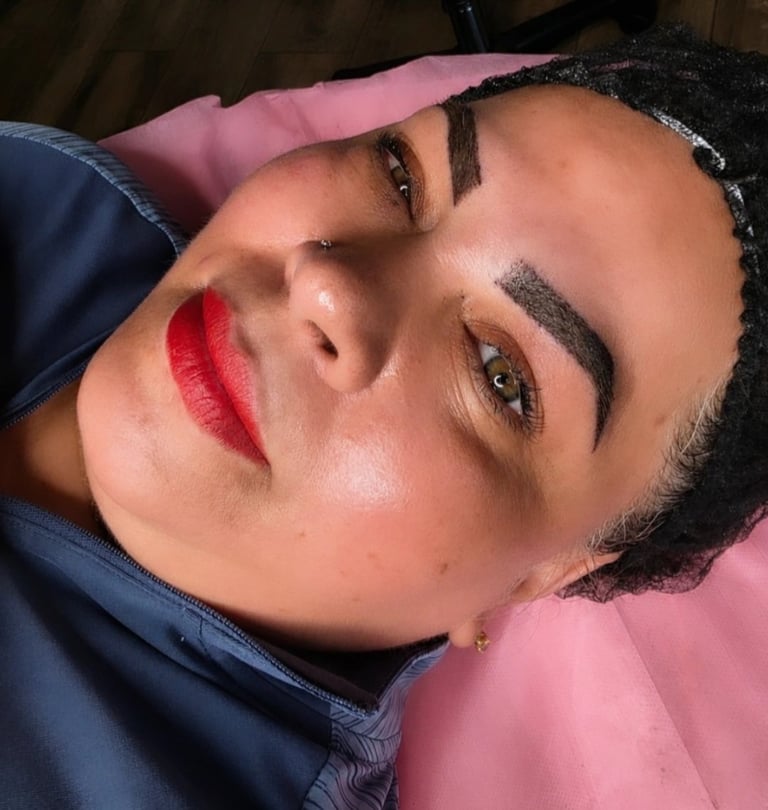 Person with dark braided hair wearing red lipstick and black eyeliner, looking upward against pink and blue background