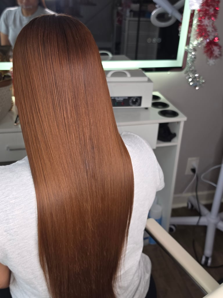 Back view of person with long, straight, copper-brown hair in a salon setting with mirrors and holiday decorations