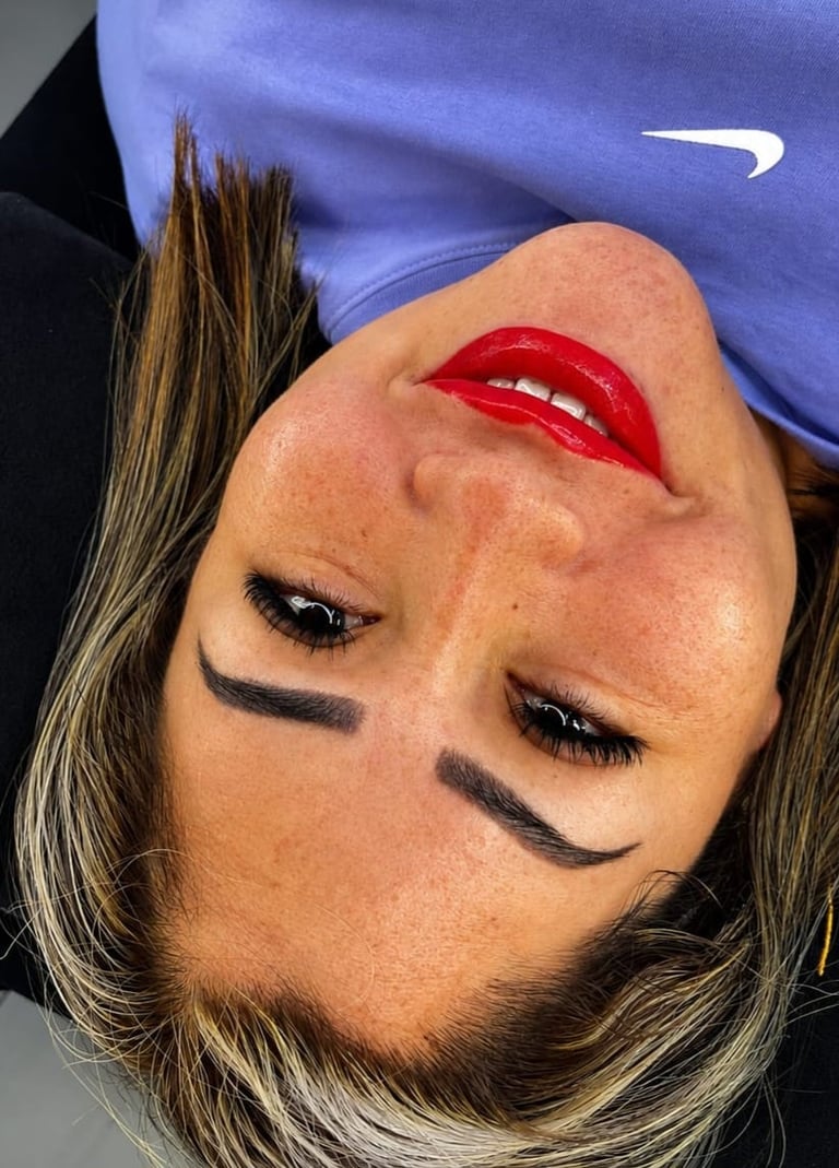 Upside-down portrait of a person with bold red lipstick, defined eyebrows, and eyeliner wearing a blue and black athletic top