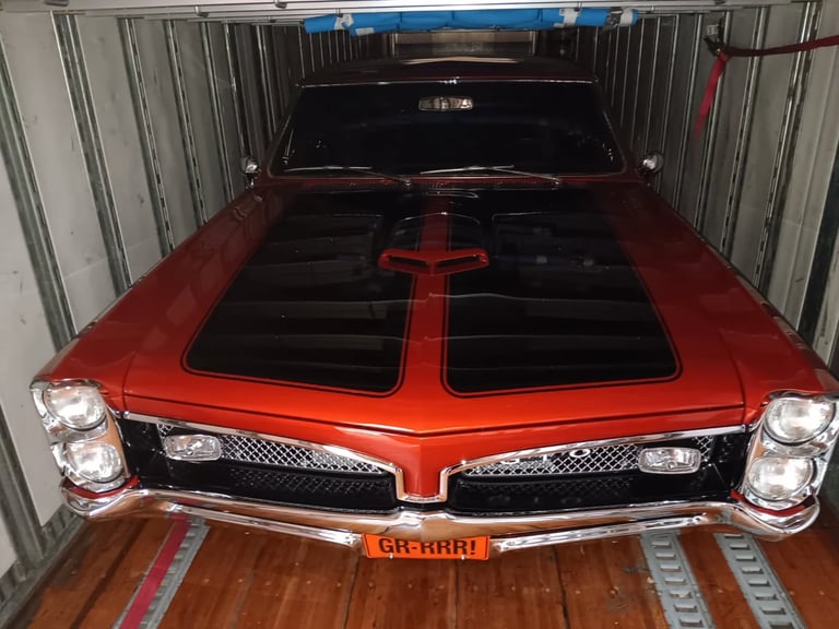 Red vintage Pontiac muscle car with black hood stripes in metal storage garage, front view with headlights visible