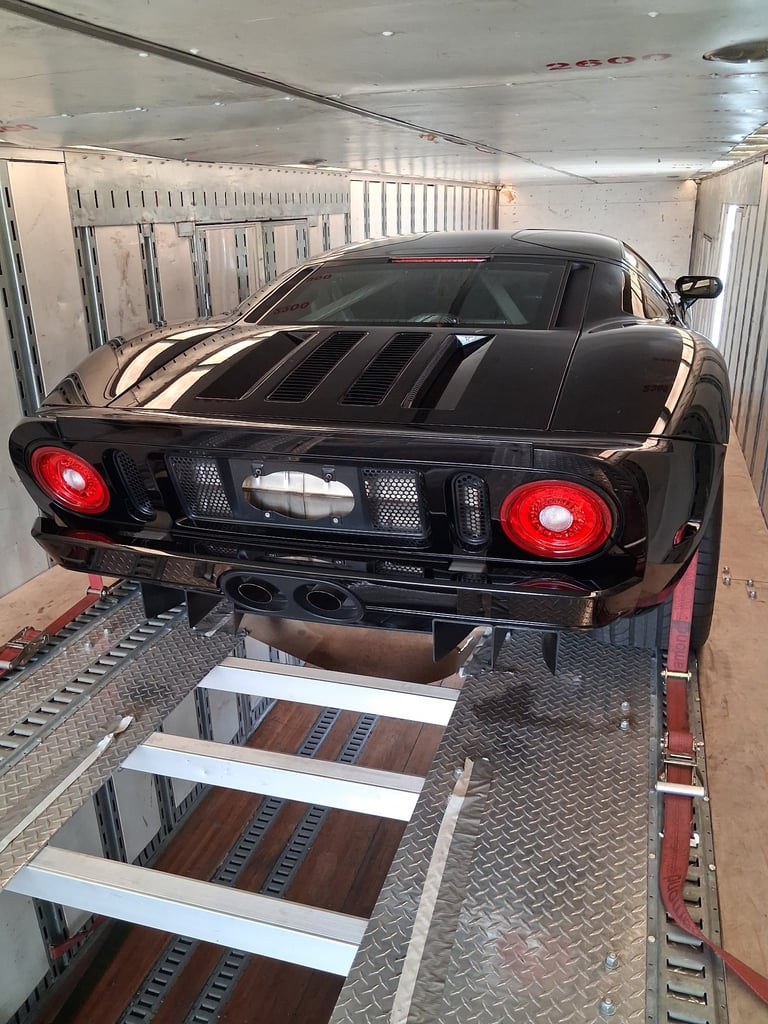 Black sports car with red taillights loaded on a white ramp inside a metal transport trailer