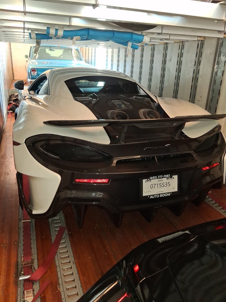 White sports car with black rear wing in an automotive workshop with blue lift and industrial ceiling