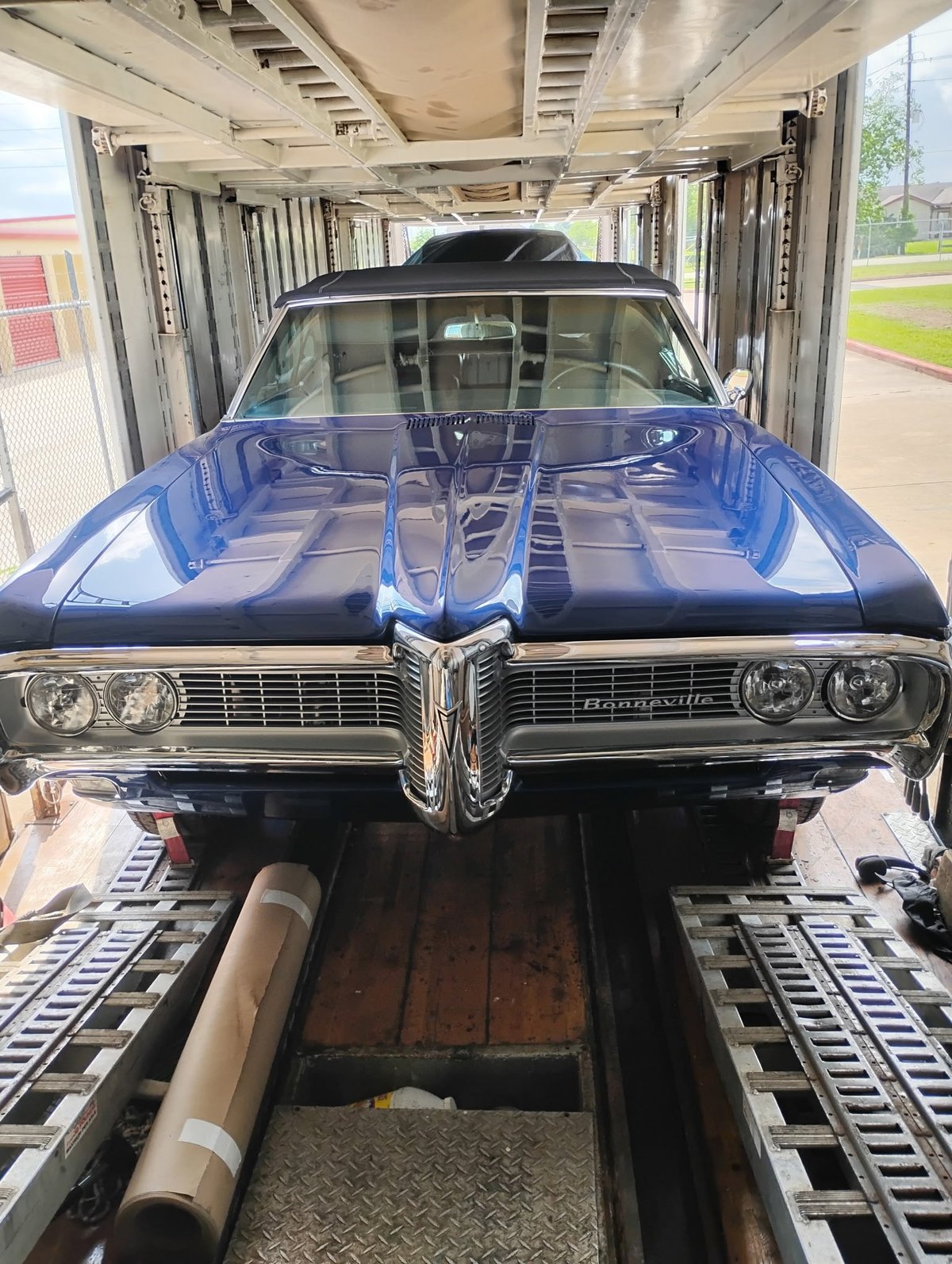 Blue and black classic car loaded in metal transport trailer, frontal view showing hood and grille