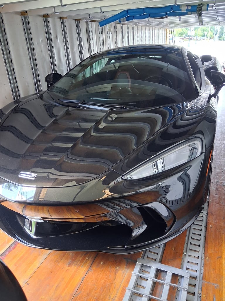 Black sports car parked in a garage bay with corrugated metal walls and fluorescent lighting