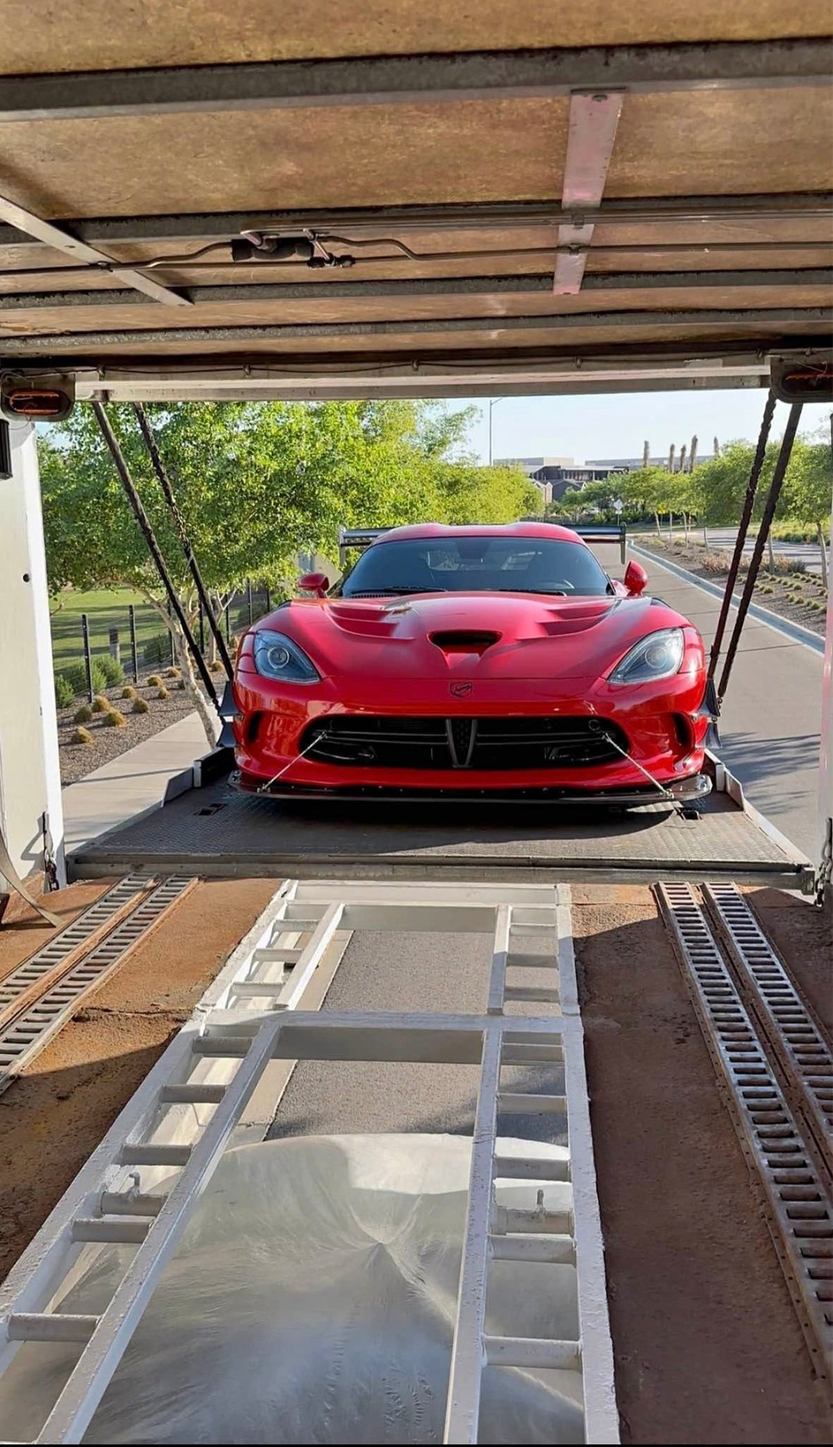 Red sports car loaded on a car transport trailer under a covered structure