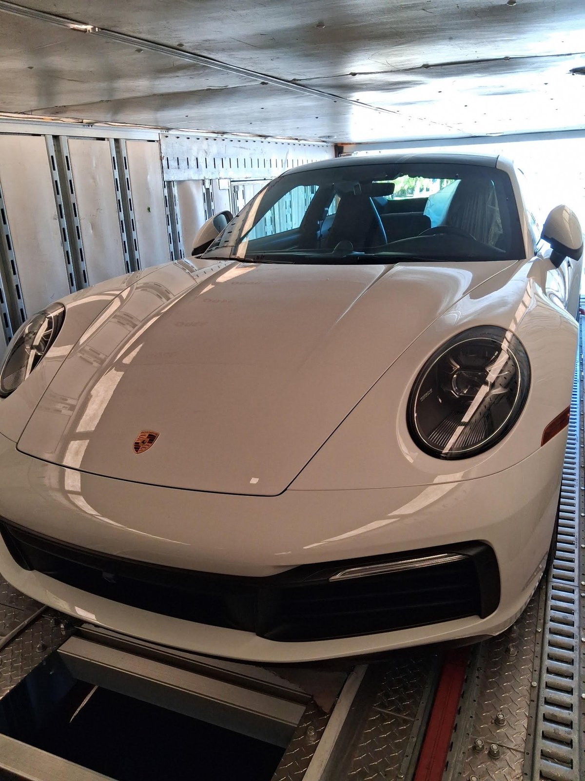 White Porsche 911 loaded in enclosed transport trailer with garage doors open