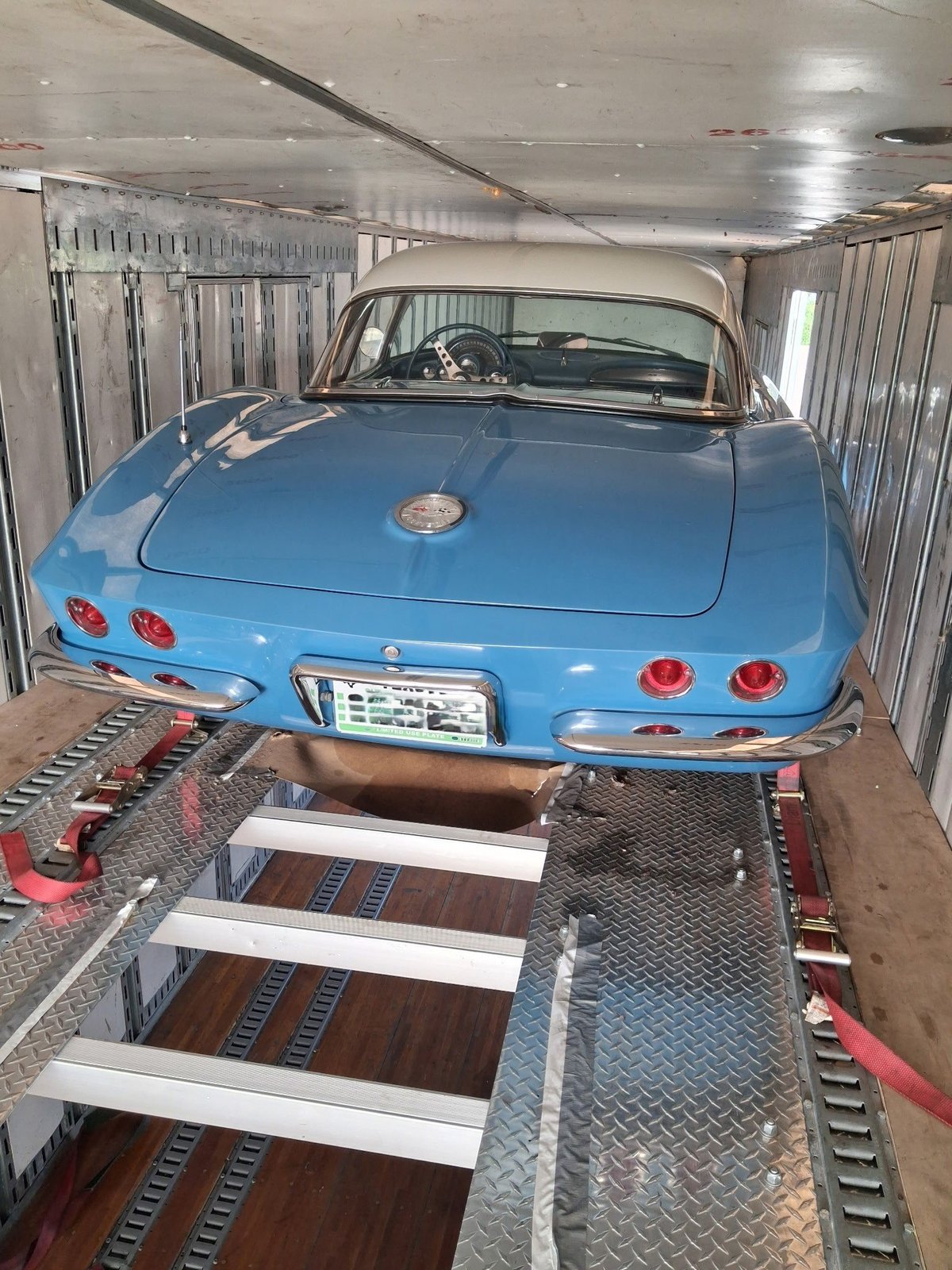 Blue vintage Corvette sports car secured on a trailer with metal tie-downs inside a transport vehicle