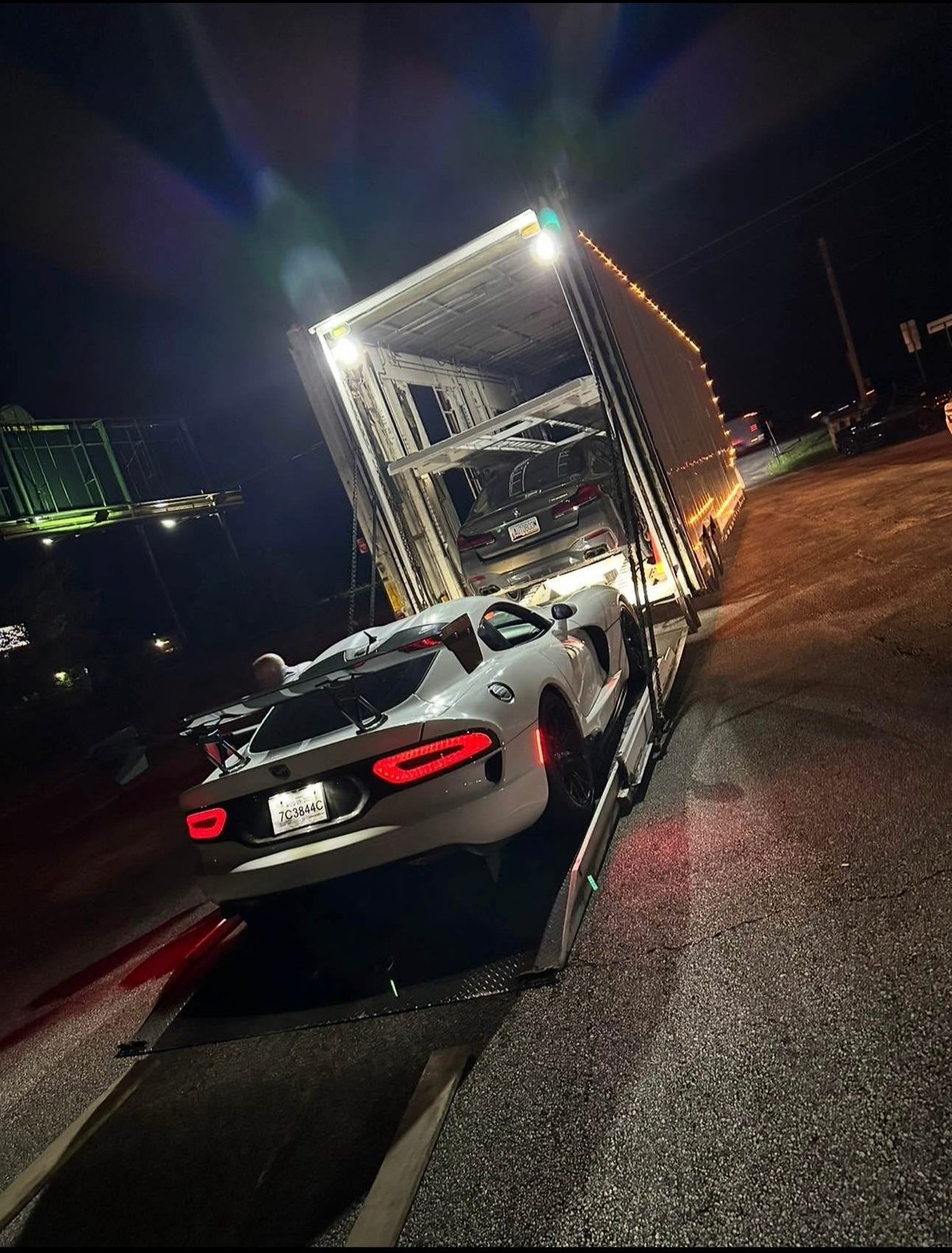 White sports car being loaded into illuminated cargo trailer at night