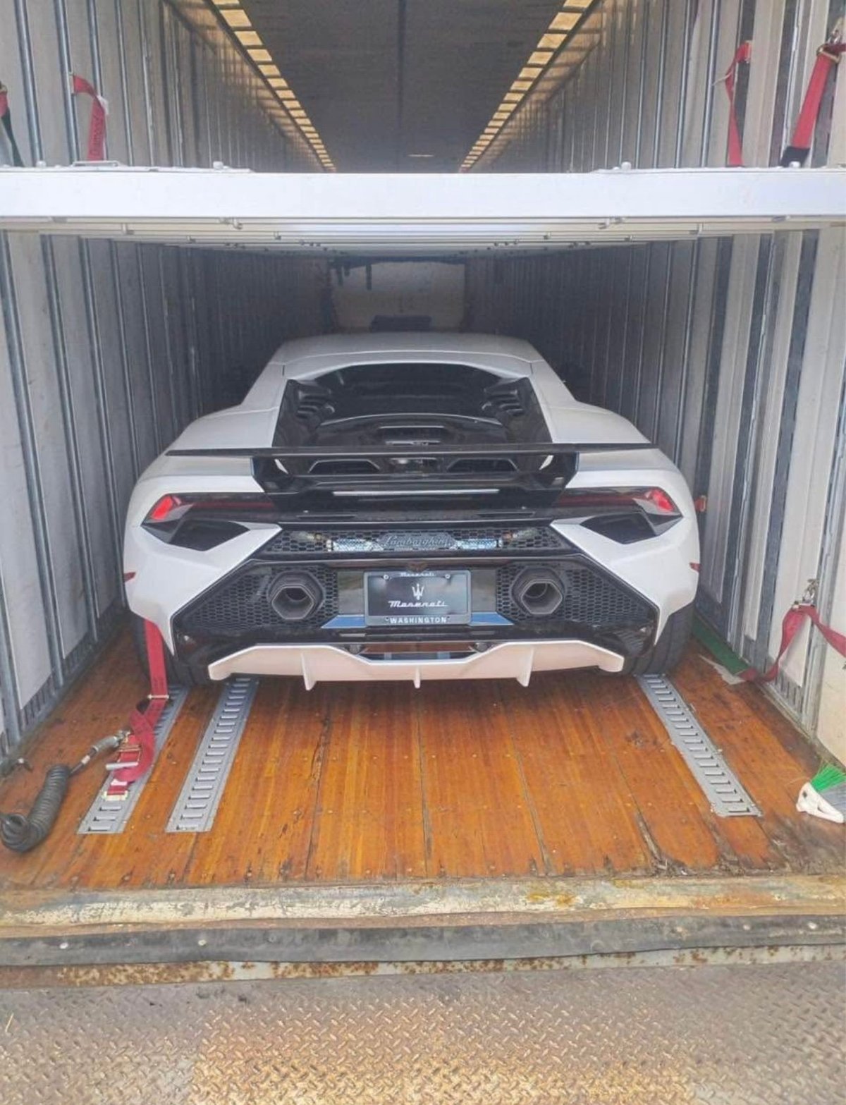 White and red sports car with open hood loaded in metal shipping container