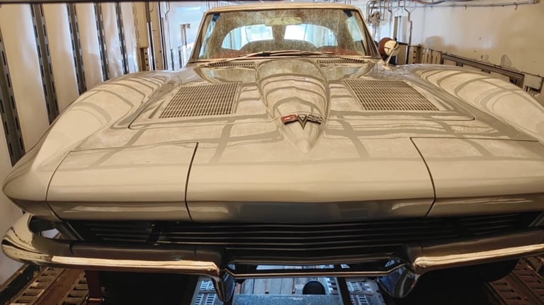 Cream-colored classic Chevrolet Corvette parked in a garage with hood up, showing detailed engine compartment and front grille