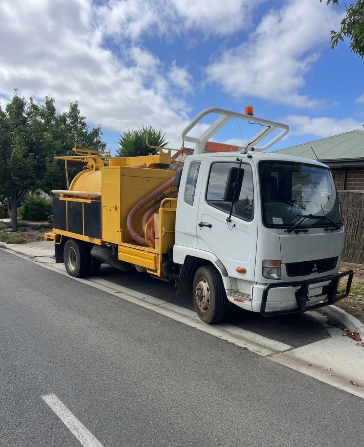 White Mitsubishi truck with yellow wood chipping equipment attached, parked on residential street under blue sky