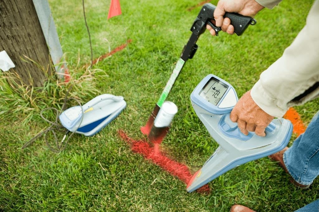 Person using soil testing equipment on grass, holding a probe and meter to measure soil composition