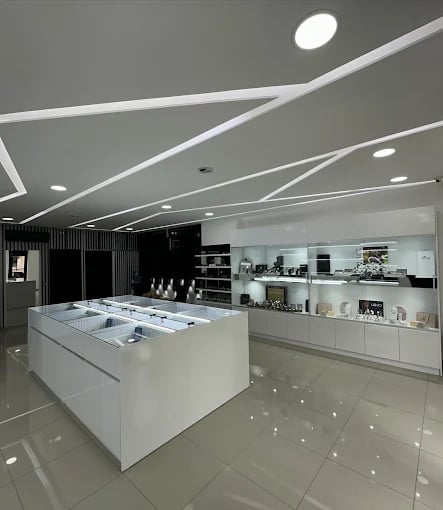 Modern minimalist retail showroom with white central display counter, black accent wall, geometric ceiling design, and recessed lighting
