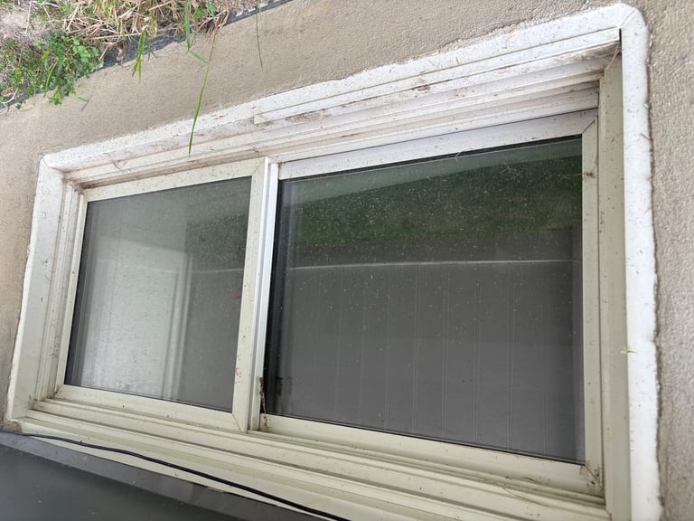 Two-panel basement window with dark mesh screens after cleaning, frames bright and glass clear