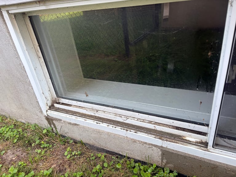 Basement window with white frame and glass pane showing dirty exterior before cleaning