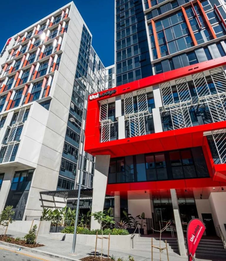 Modern residential buildings with white and orange facades, featuring a bold red entrance structure and ground-level landscaping