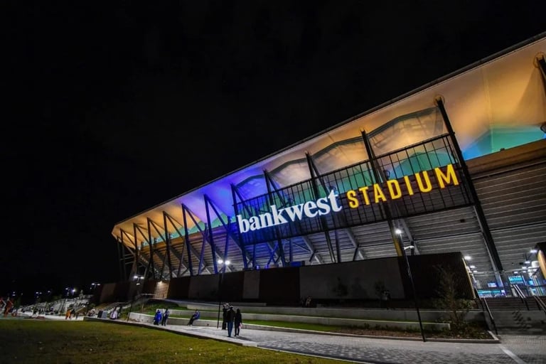 Bank West Stadium exterior lit up at night with illuminated signage and distinctive architectural features, showing the main entrance facade