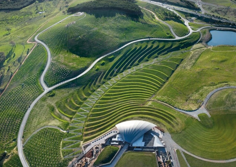 Aerial view of terraced vineyard hillsides with winding roads and a modern dome-shaped winery building nestled in the valley