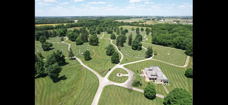 Aerial view of a vineyard estate with rows of grapevines, winding paths, and a white building surrounded by green fields and trees.