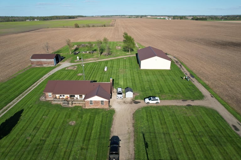 Aerial view of a rural farm with brick house, two barns, grain silos, and surrounding crop fields
