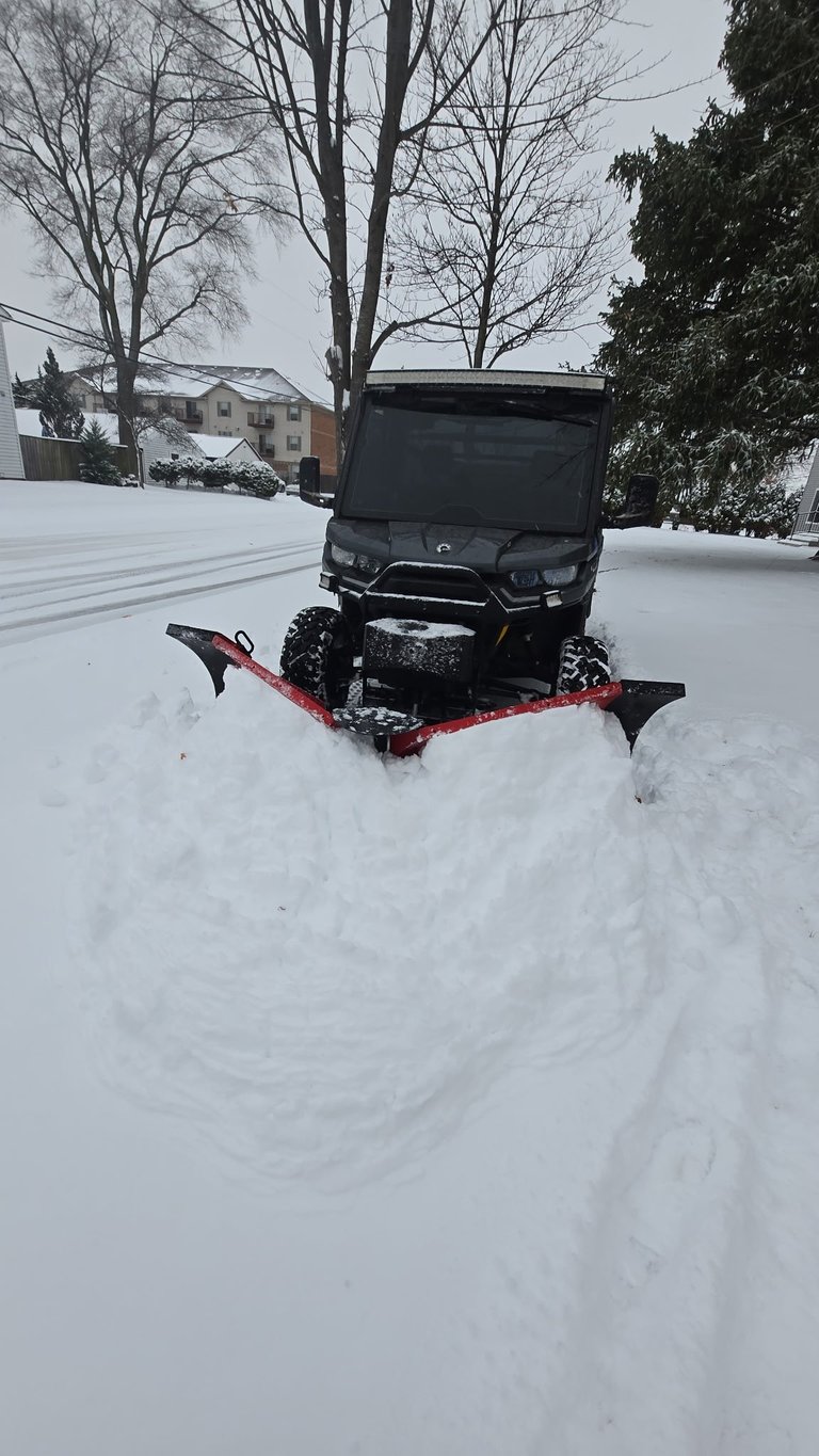 ATV with red snow plow attachment clearing snow in a snowy residential neighborhood